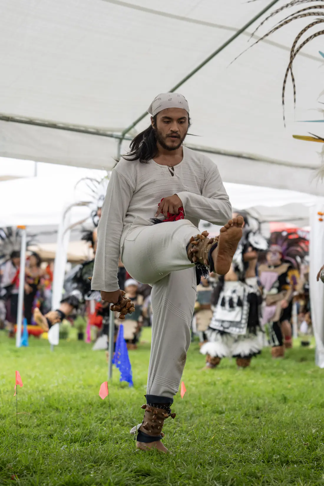 A dancer in white executes a high kick with feathered anklets