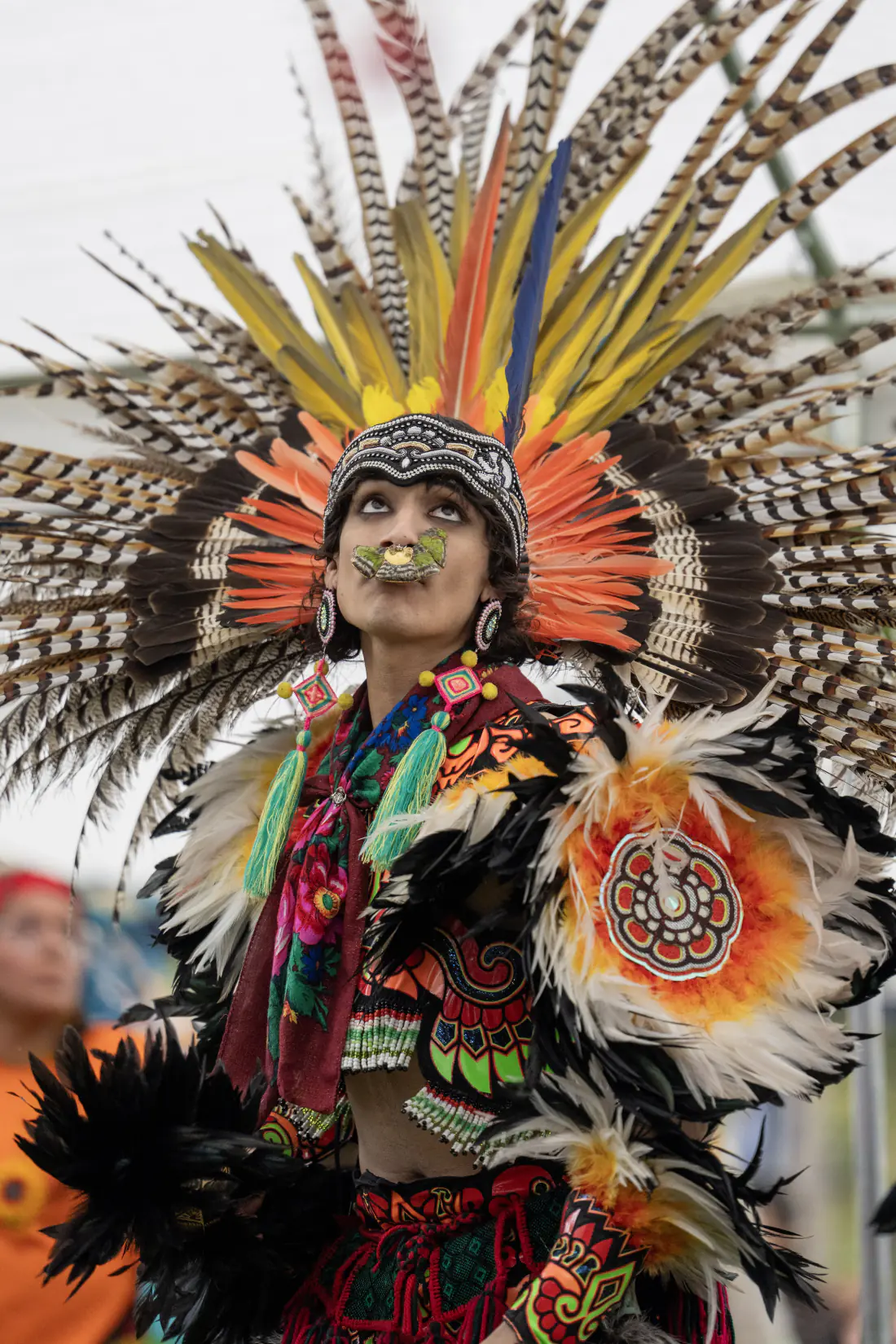 Portrait of a dancer in a yellow and orange feather headdress and beaded cap, eyes raised