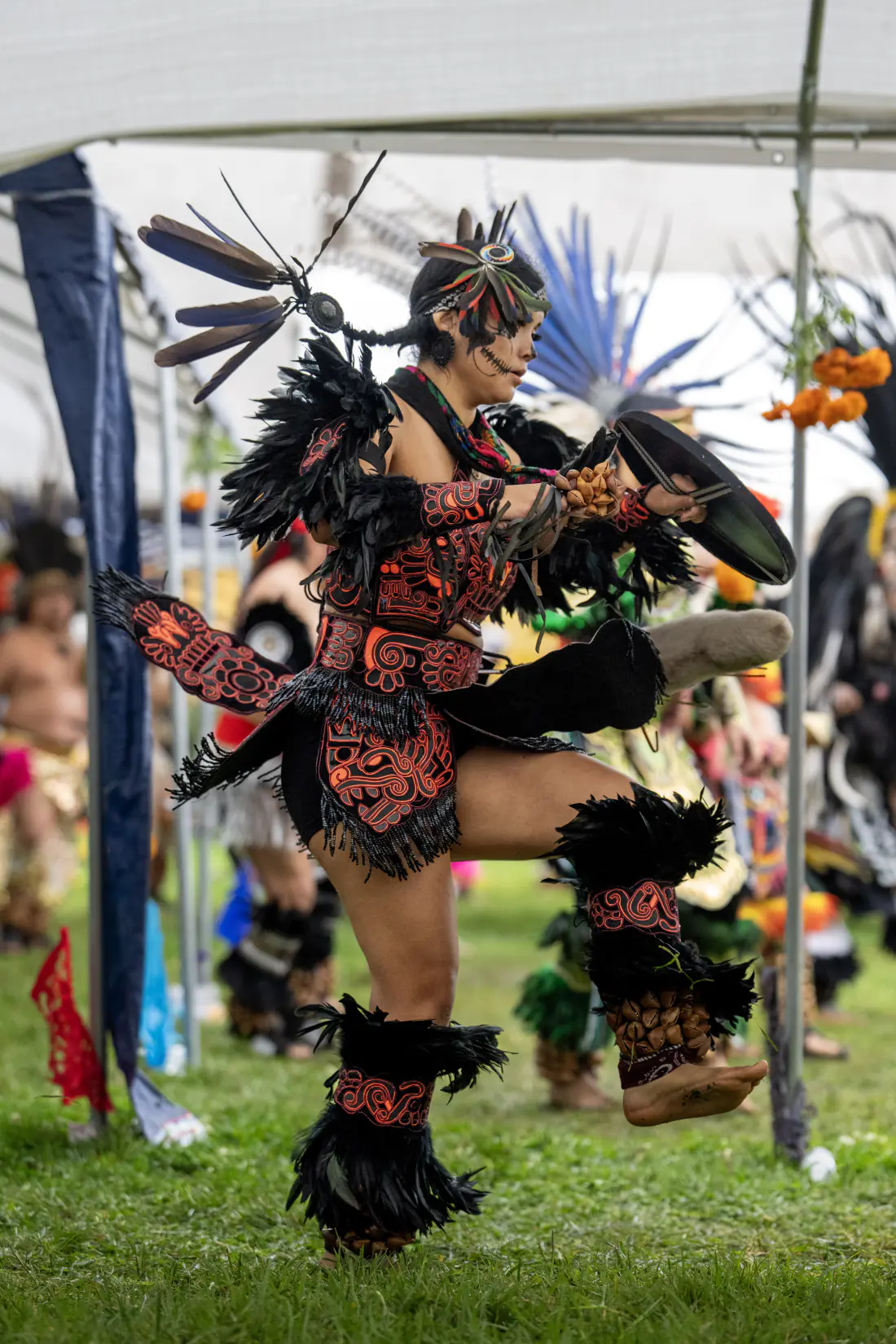 A dancer in black and orange beaded regalia mid-kick, fully airborne
