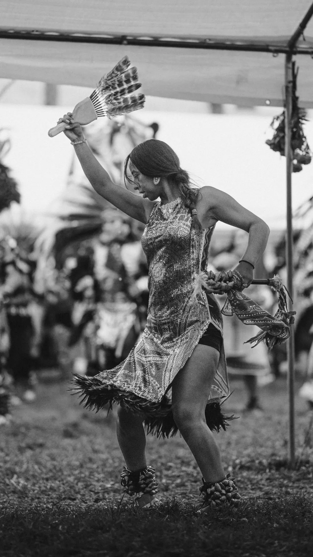 A dancer in a sequined dress spins with a feather fan raised overhead, black and white