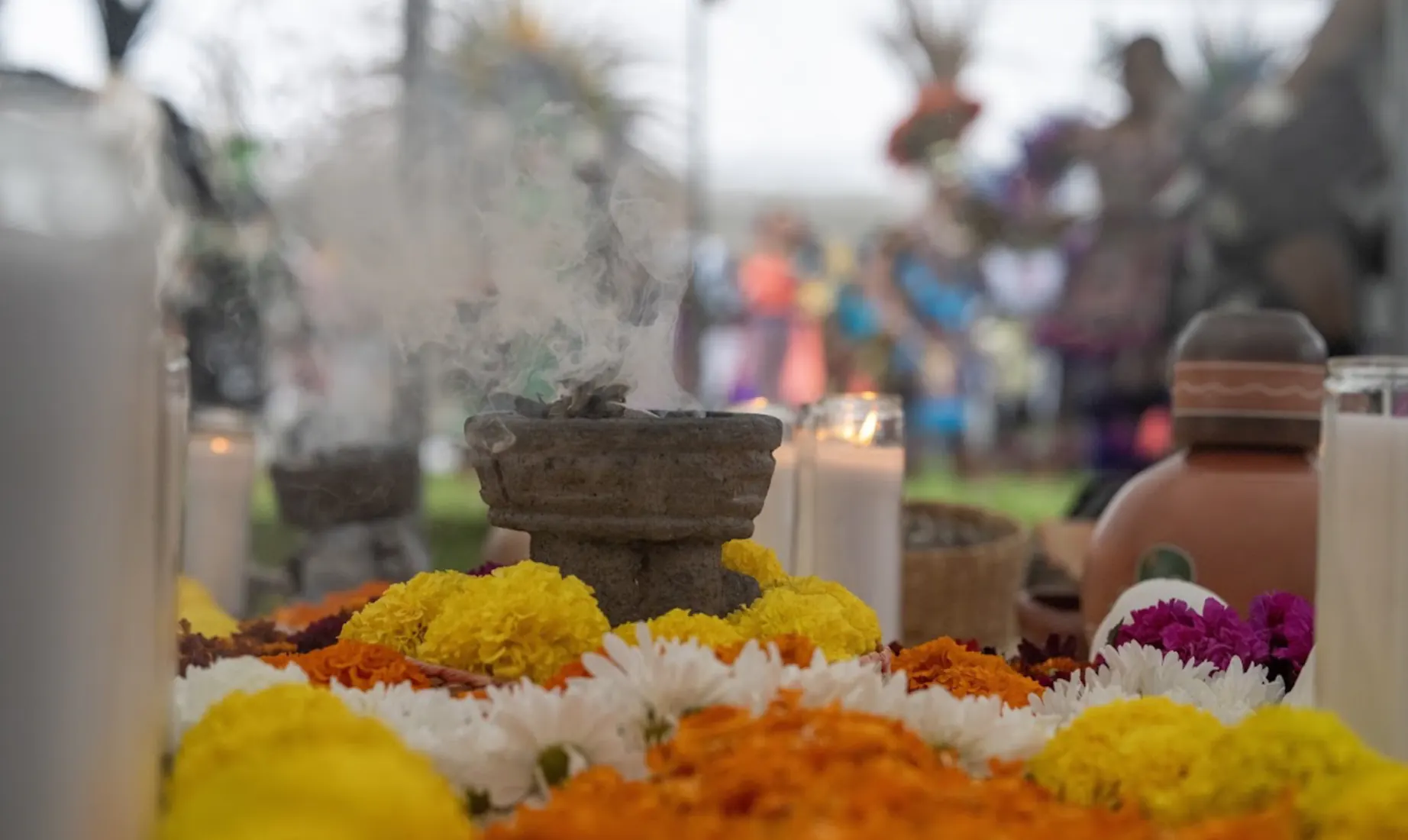 A close view of the copal burner and candles at the altar, community gathered beyond