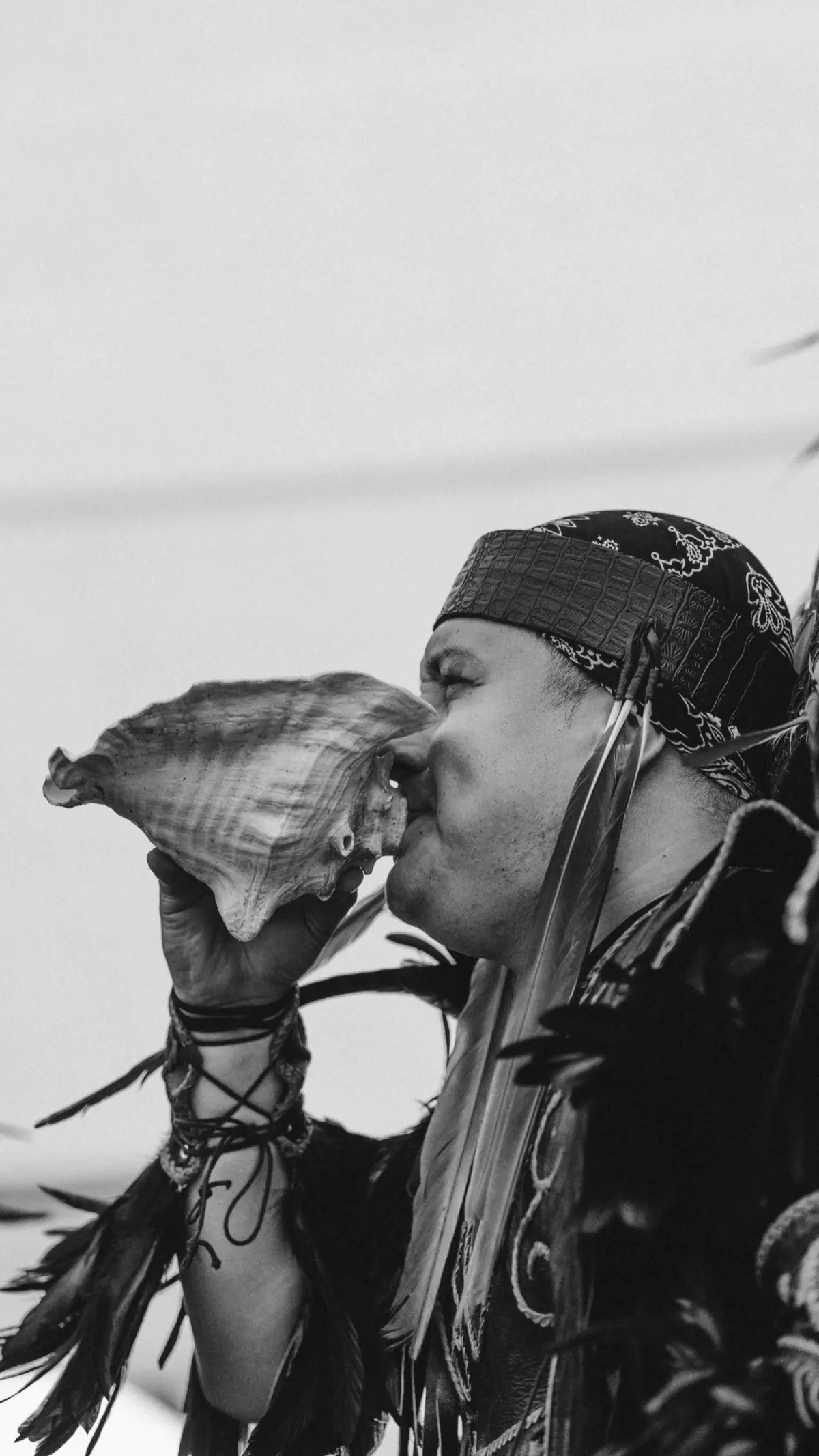 Black and white portrait of a dancer in profile blowing a conch shell